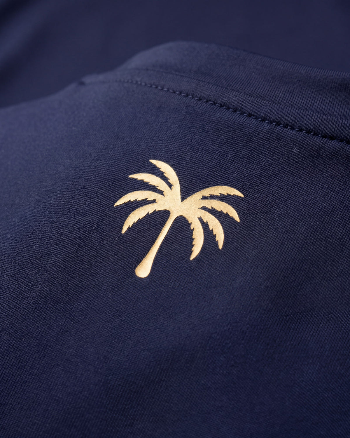 Palmera dorada estampada sobre el tejido técnico azul marino del rashguard FIJI