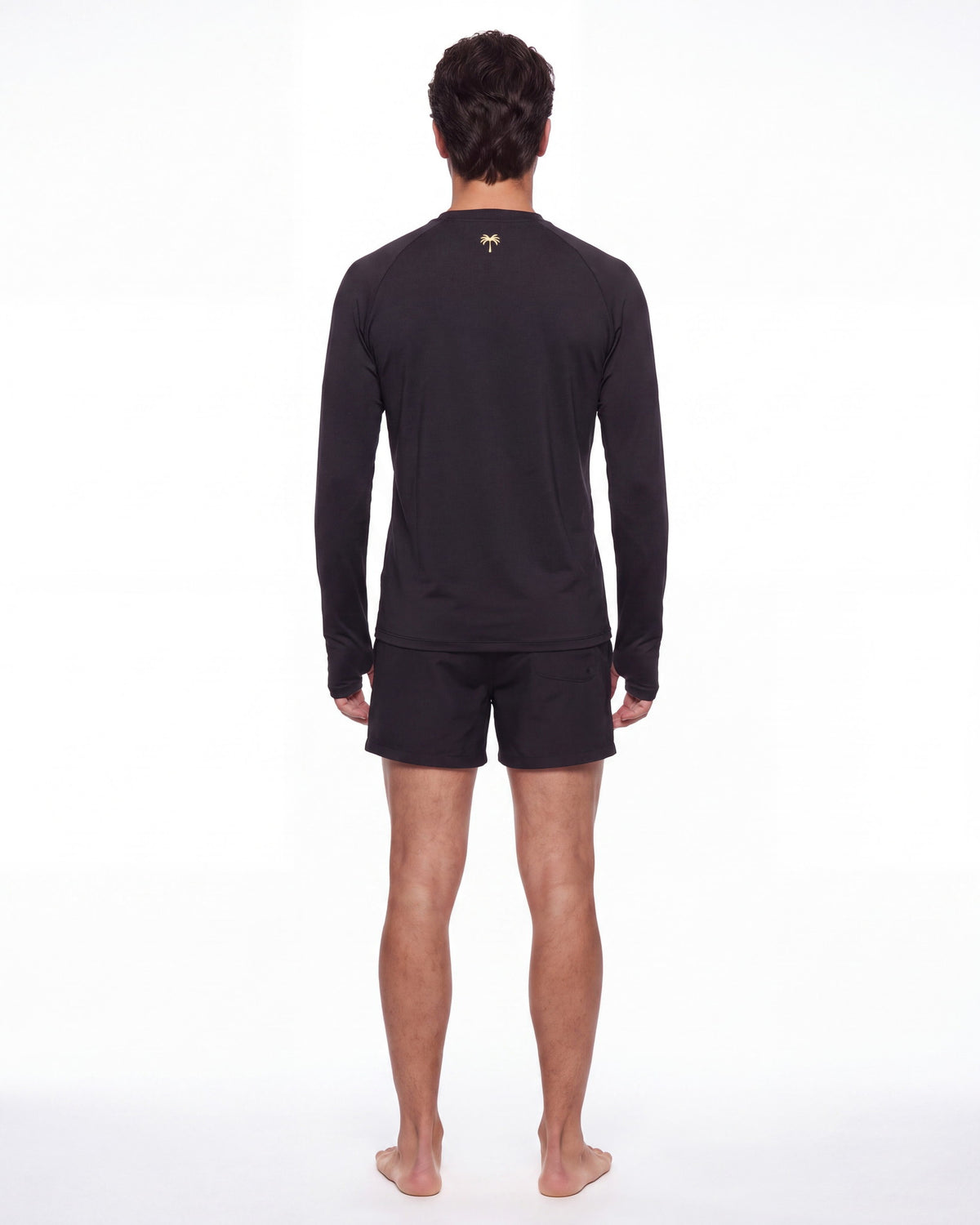 Hombre de espaldas con rashguard FIJI negro; la palmera dorada queda centrada