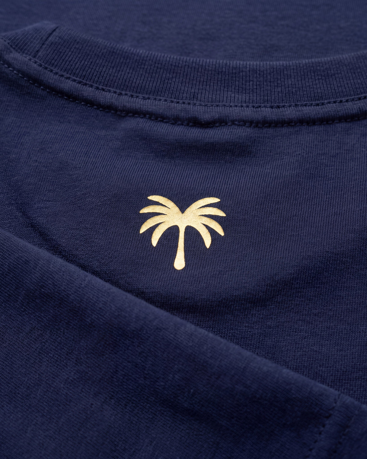 Palmera dorada estampada sobre el tejido azul marino de la camiseta KAI