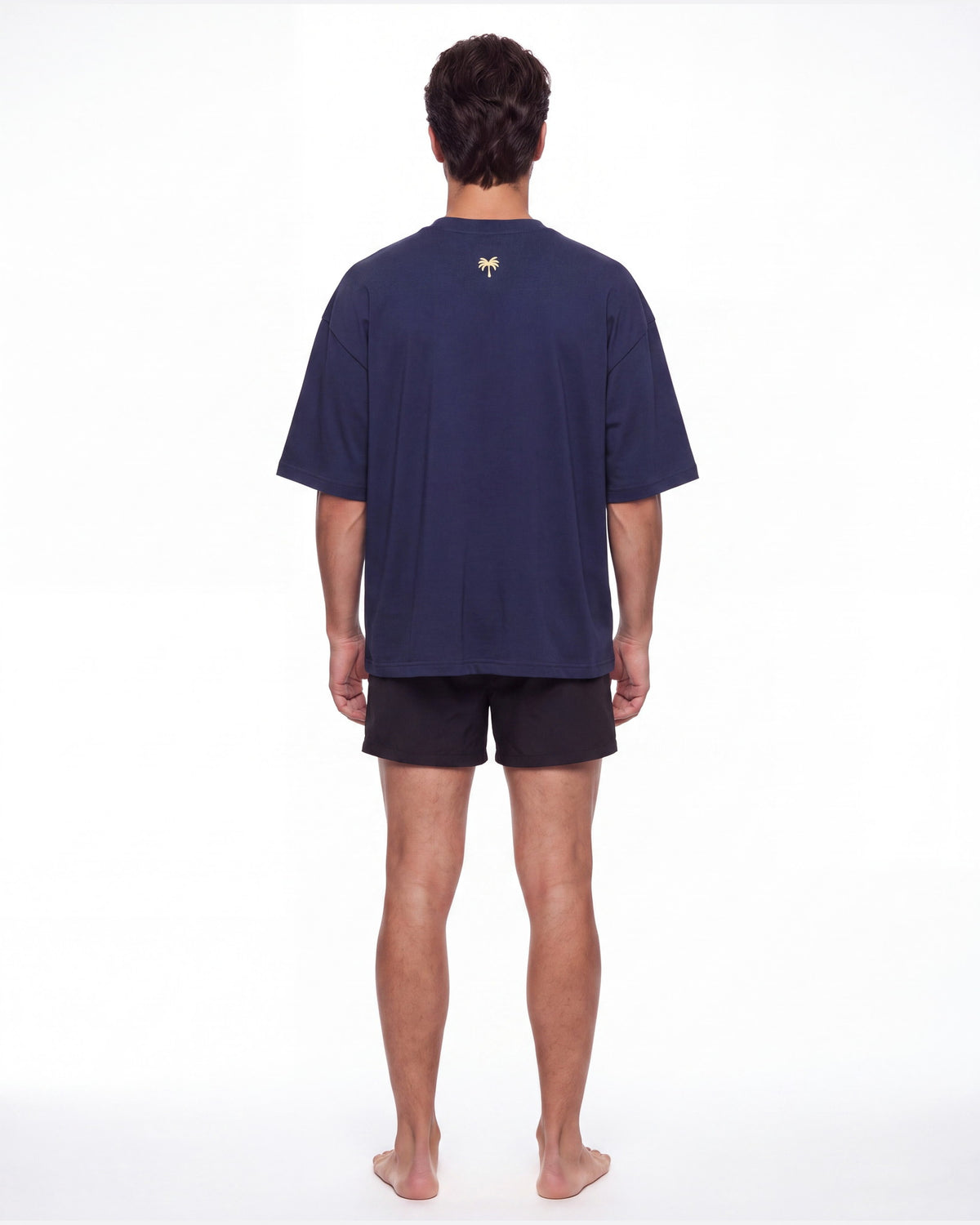 Hombre de espaldas con camiseta KAI azul marino; la palmera dorada queda centrada