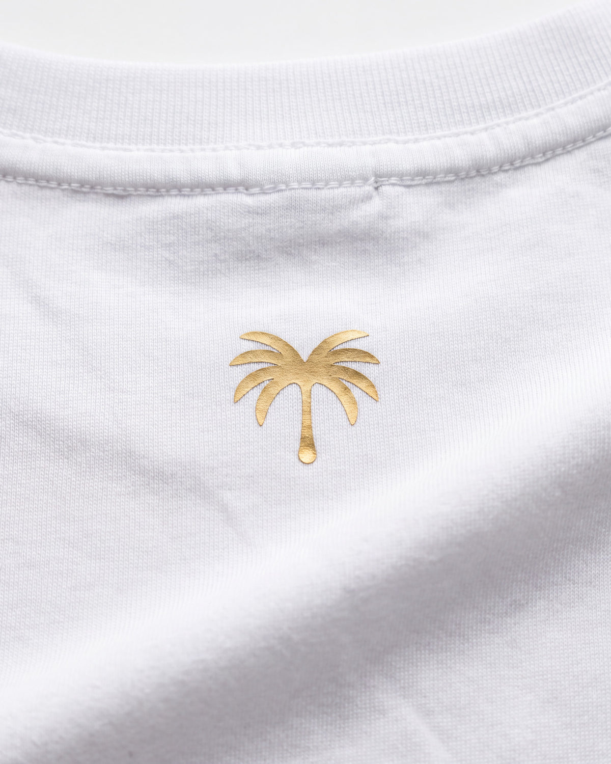 Palmera dorada estampada sobre el tejido blanco de la camiseta KAI