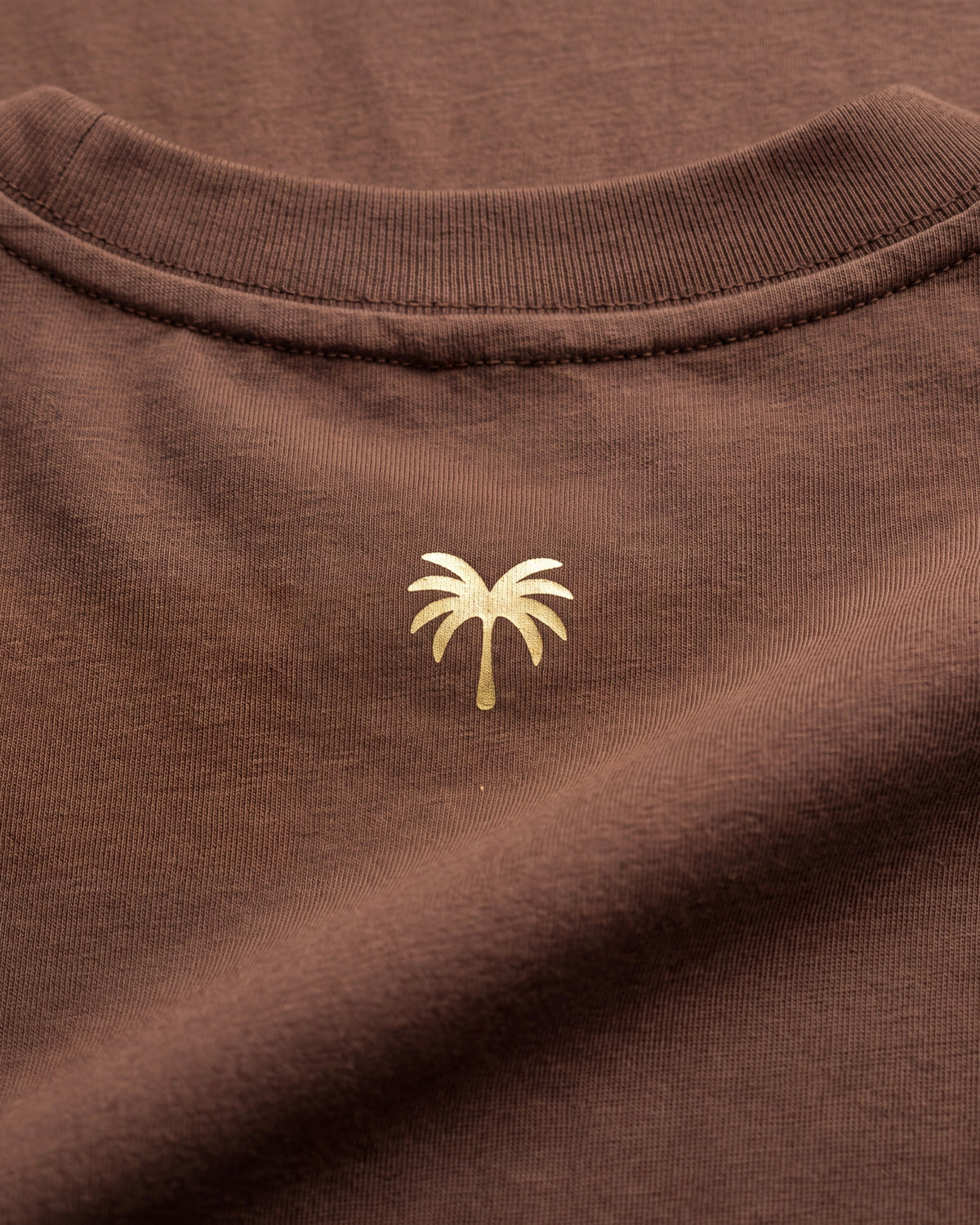 Palmera dorada estampada sobre el tejido café de la camiseta KAI