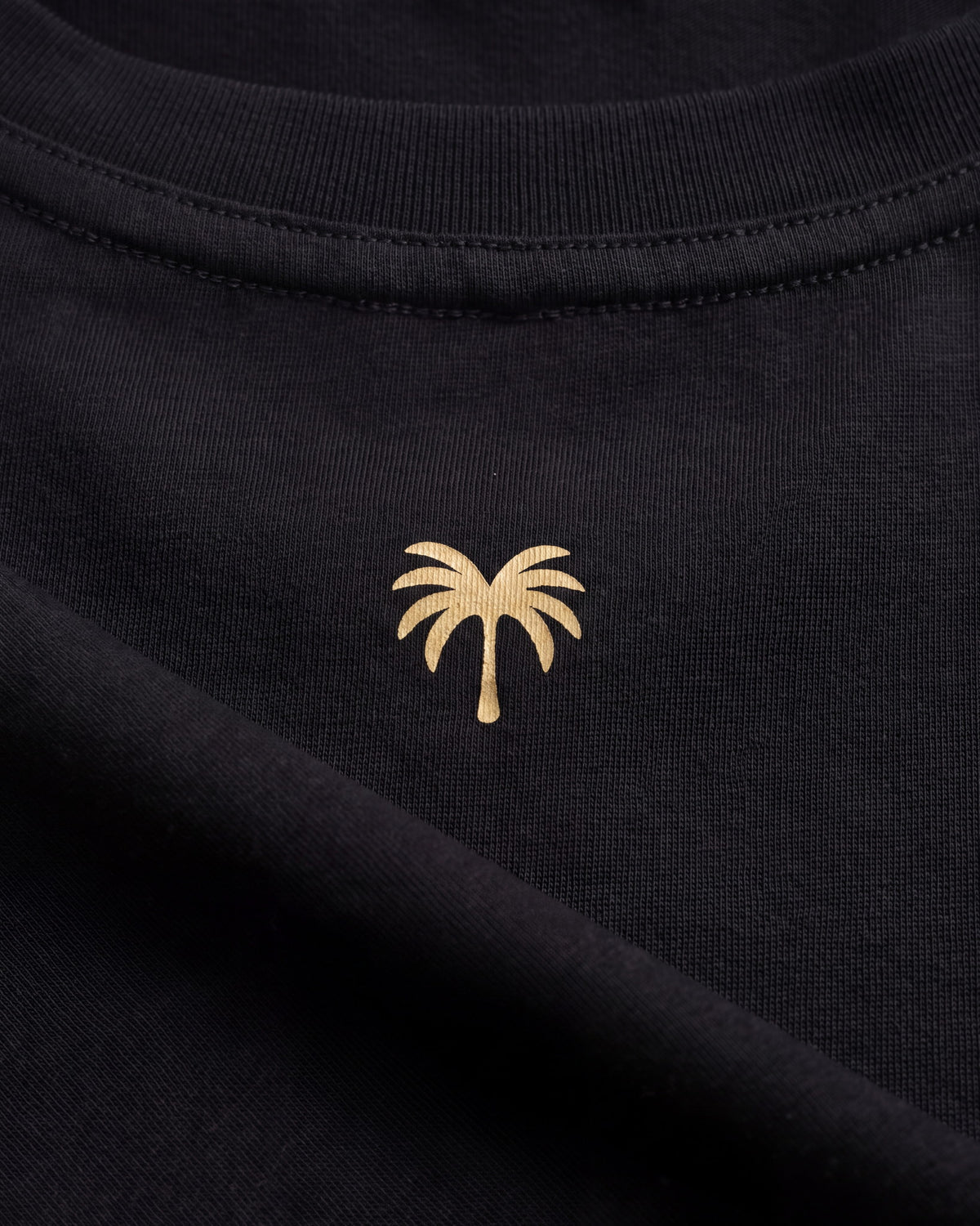 Palmera dorada estampada sobre el tejido negro de la camiseta KAI
