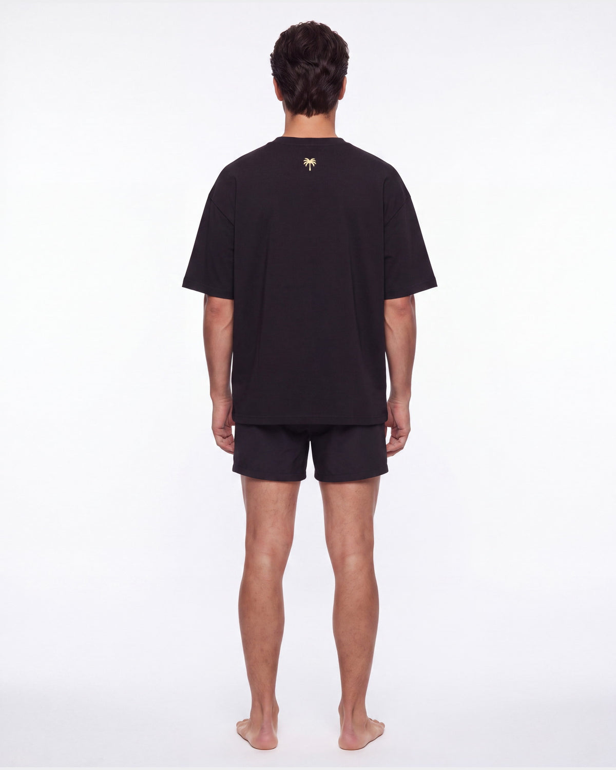 Hombre de espaldas con camiseta KAI negro; la palmera dorada queda centrada
