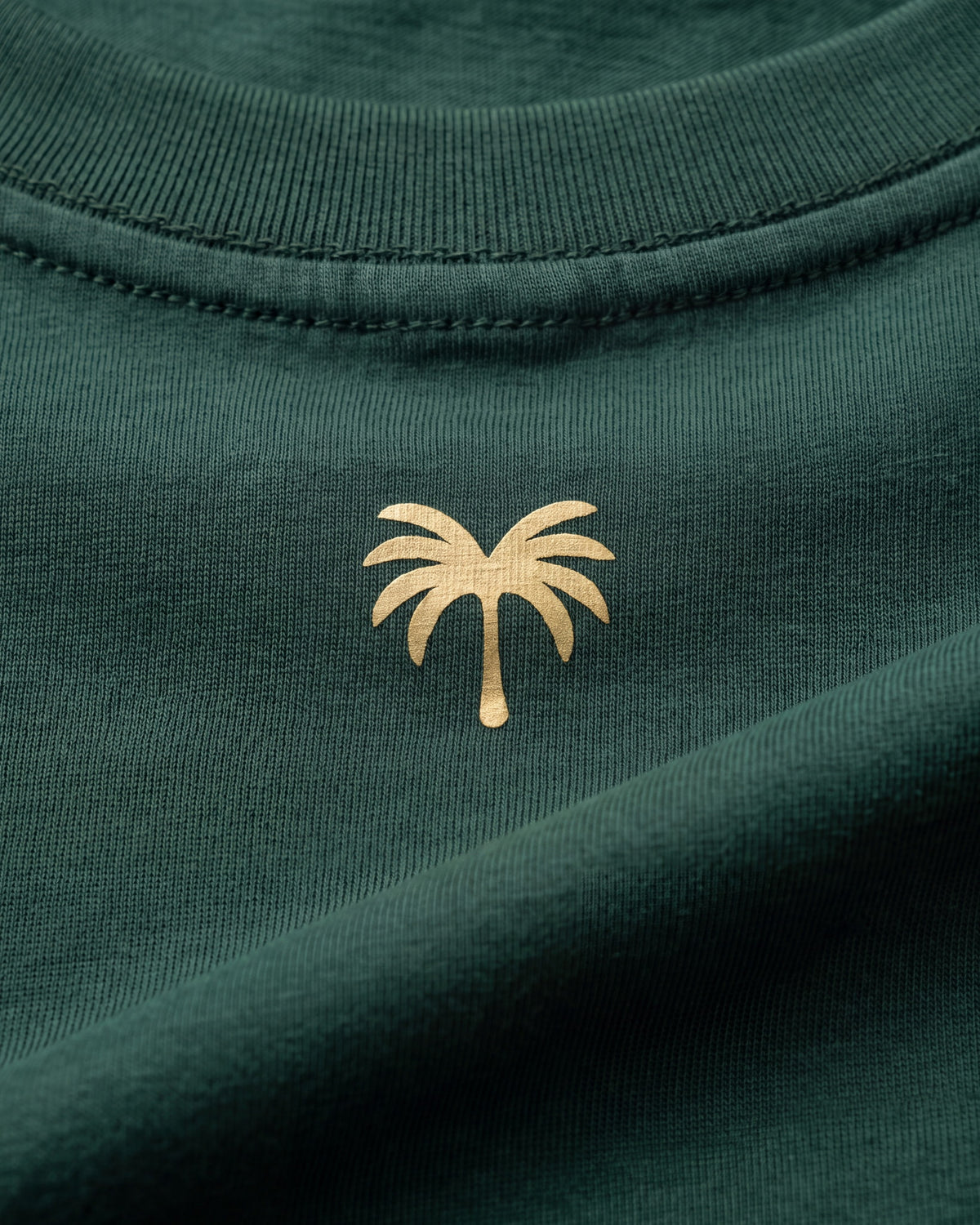 Palmera dorada estampada sobre el tejido verde botella de la camiseta KAI